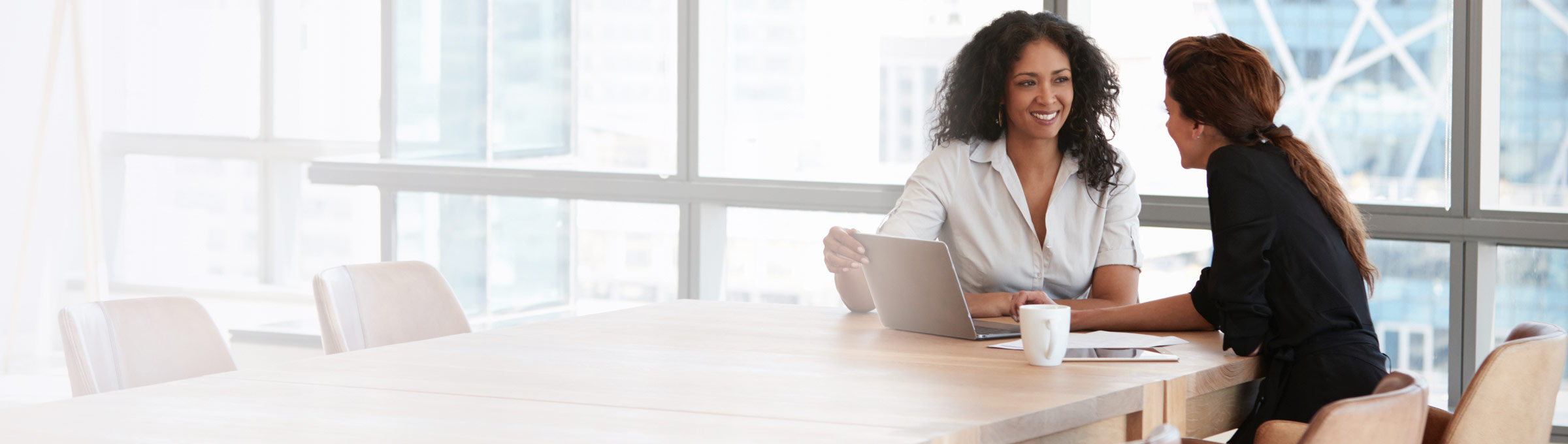 Two women sitting at conference room table with laptop